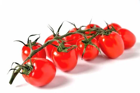 A branch of red cherry tomatoes sharp in front and blurred from behind on a w Foto stock