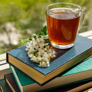 Branches of blooming bird cherry tree and a glass cup with tea on a stack of Foto stock
