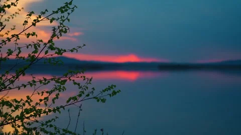 Branches of trees and a beautiful sunset on the background of a calm lake. Vidéo 334648018