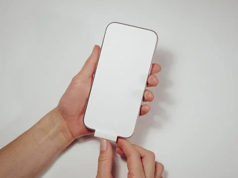 A brand new iPhone 16 about pink titanium in women's hands. A white sticker Stock Photos