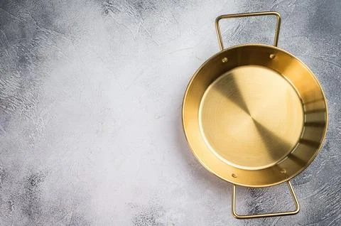 Brass colored cooking pan on dramatic grey backdrop, flat lay kitchen equip.. Stock Photos