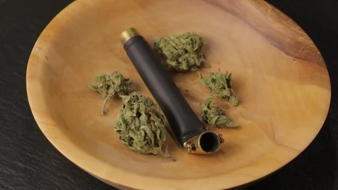 Brass smoking pipe with multiple sativa and indica weed buds in wooden plate on Vidéo 124507527