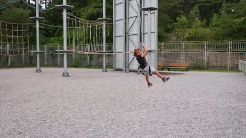 A brave boy confidently zips down zip lines in a rope park, feeling the Stock Footage 250880820
