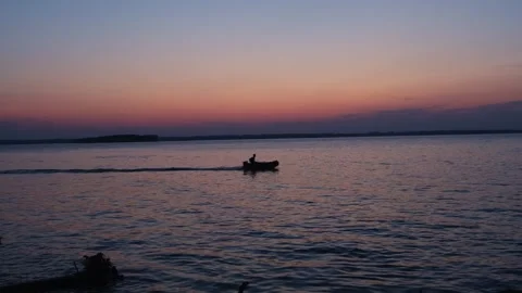A brave man floats on an inflatable motorized boat along the river at sunset. Stockbeeldmateriaal 247225862