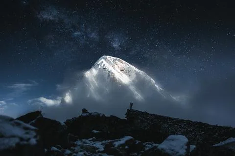 Brave solo mountain traveler stand in front of huge snowy mountain and starry Stock Photos