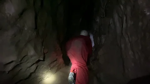 A brave tourist squeezing through a small hole on a caving adventure 스톡 동영상 122099837