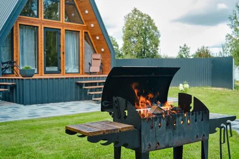 Brazier with burning wood on the background of a triangular house Stock Photos