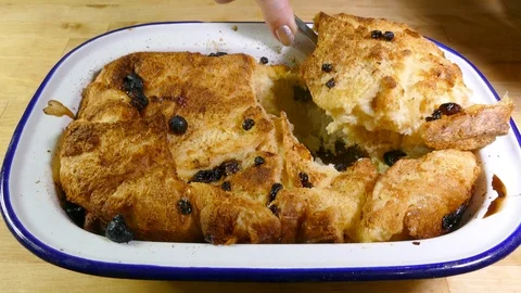 Bread and butter pudding dessert, being served from a baking dish to a bowl. Video stock 98045271