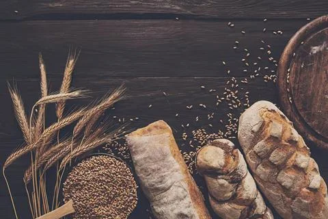 Bread and grains on dark rustic surface with wheat stalks Stock Photos