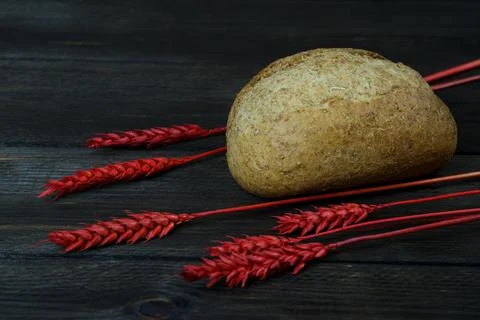 Bread and red spikelets on black wooden table Stock Photos