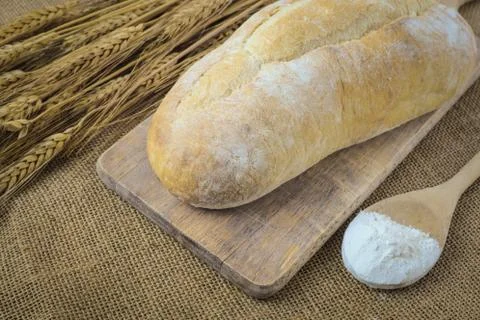 Bread on bread board with wheat and flour filled spoon on burlap background Stock Photos