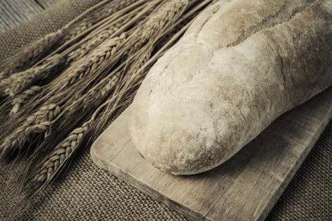 Bread on bread board with wheat on burlap background Stock Photos