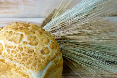 Bread brick and a bunch of wheat spikelets on a wooden background. Stock Photos