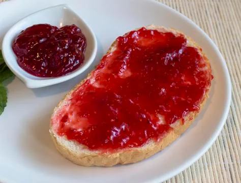 Bread with butter and raspberry jam on a white plateau. Stock Photos