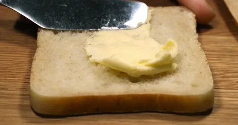 Bread with butter. Knife smearing soft butter on slice of bread, close up vie Stock Footage 148775943