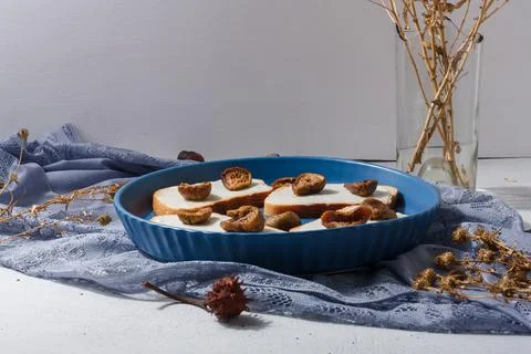 Bread with cheese and figs on blue plate, vase of dry flowers on background. Stock Photos