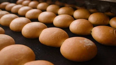 Bread comes out of the oven in close-up on a conveyor belt and is sprayed with Stock-Footage 129272294