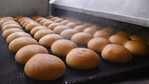 Bread comes out of the oven in close-up on a conveyor belt and is sprayed with Stock Footage 130718810