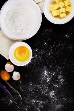 Bread concept a bowl of raw egg, cubes of butter, flour put on the black scen Stock Photos
