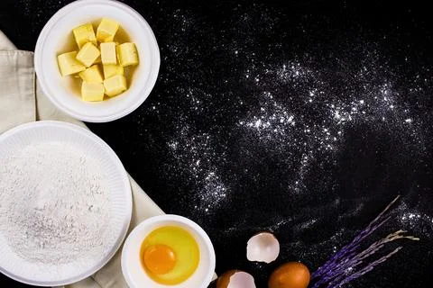 Bread concept a bowl of raw egg, cubes of butter, flour put on the black scen Stock Photos