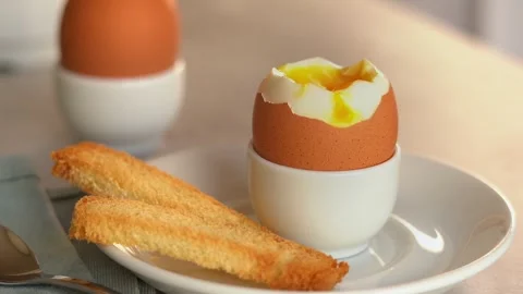 Bread crouton dips in soft-boiled egg. Chicken yolk flows down egg. Breakfast Stock Footage 302648151