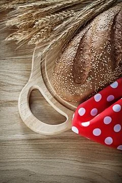 Bread cutting board rye ears red tablecloth on wooden background Stockfoto's