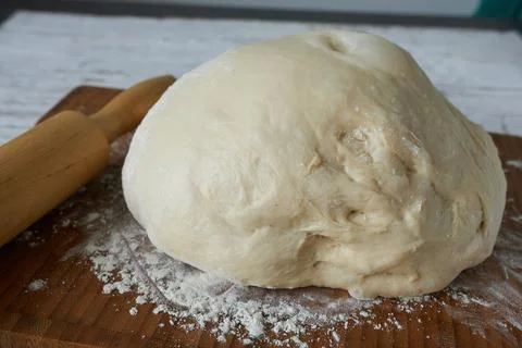 Bread dough and rolling pin on a wooden board with flour. Stock Photos