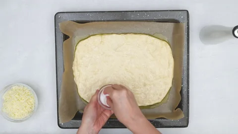 Bread dough on a baking pan. Chef topping bread dough with salt. Stock Footage 145789184