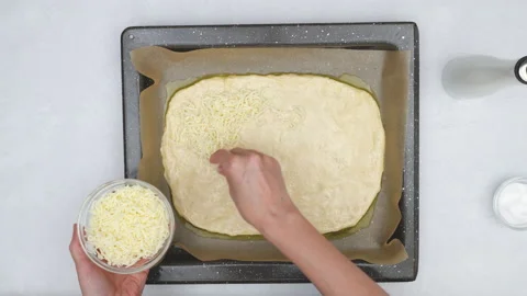 Bread dough on a baking pan. Chef topping bread dough with mozzarella.  Stock Footage 145790067