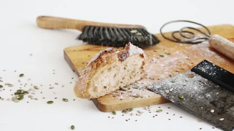 Bread flour falling onto sourdough bread and baking tools on cutting board Stock Footage 195999229