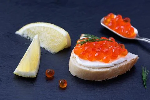 Bread with fresh cream cheese, red caviar and lemon on black slate plate Stockfoto's