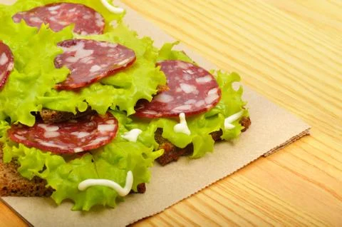 Bread with ham and lettuce on paper, on wooden background Stock Photos