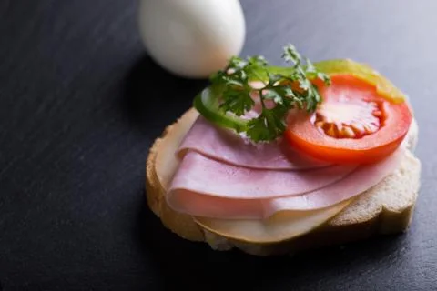 Bread with ham, eggs, tomatoes and green pepper on black background. Stock Photos