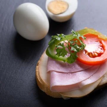 Bread with ham, eggs, tomatoes and green pepper on black background. Stock Photos