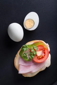 Bread with ham, eggs, tomatoes and green pepper on black background. Stock Photos
