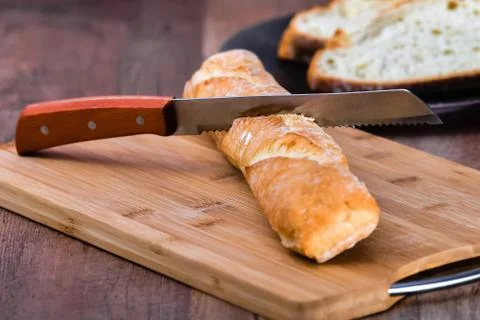 Bread knife stuck in a loaf of bread on a wooden tray on a wooden table Stock Photos