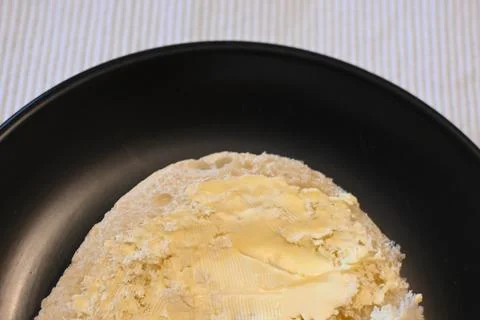 Bread roll with margarine on a black plate 스톡 사진