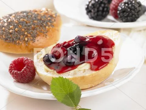 A bread roll spread with butter and berry jam Stock Photos