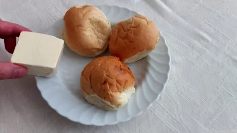 Bread Rolls and Butter Block on White Plate Over Soft Tablecloth Surface Stock-Footage 326653777