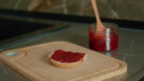 Bread slice topped with raspberry jam on a wooden chopping board in the kitchen 스톡 동영상 320951940