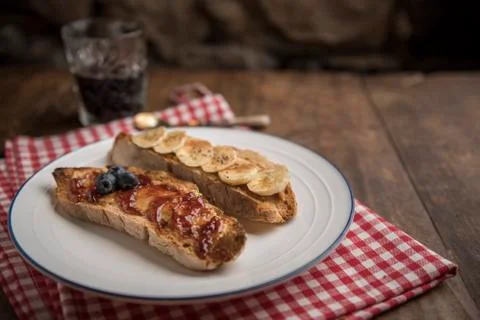 Bread slices on rustic table with peanut butter, banana and strawberry jam Stock Photos