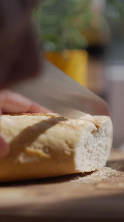 Bread slicing closeup, hand cuts loaf with serrated knife on cutting board Stock Footage 336863500