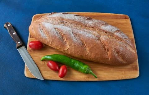 Bread, tomatoes, chilli pepper and a knife lie on the chopping board, shallow Stock Photos
