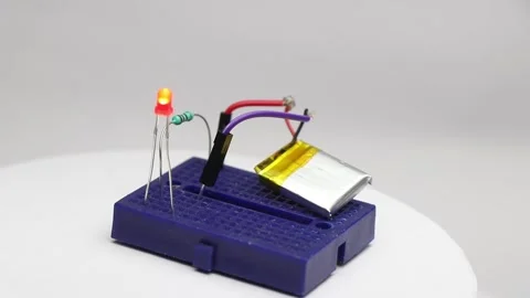 Breadboard with small red LED glowing connected to lithium polymer battery Stock Footage 345885488