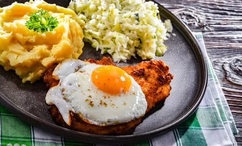 Breaded chicken cutlet served with fried chicken egg, potatoes and cabbage Stock Photos
