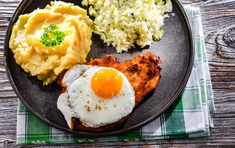 Breaded chicken cutlet served with fried chicken egg, potatoes and cabbage Stock Photos