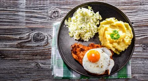 Breaded chicken cutlet served with fried chicken egg, potatoes and cabbage Stock Photos