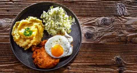 Breaded chicken cutlet served with fried chicken egg, potatoes and cabbage Stock Photos