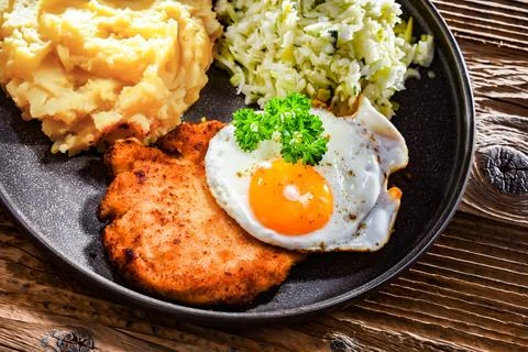 Breaded chicken cutlet served with fried chicken egg, potatoes and cabbage Stock Photos