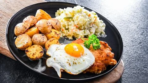 Breaded chicken cutlet served with fried chicken egg, potatoes and cabbage Stock Photos